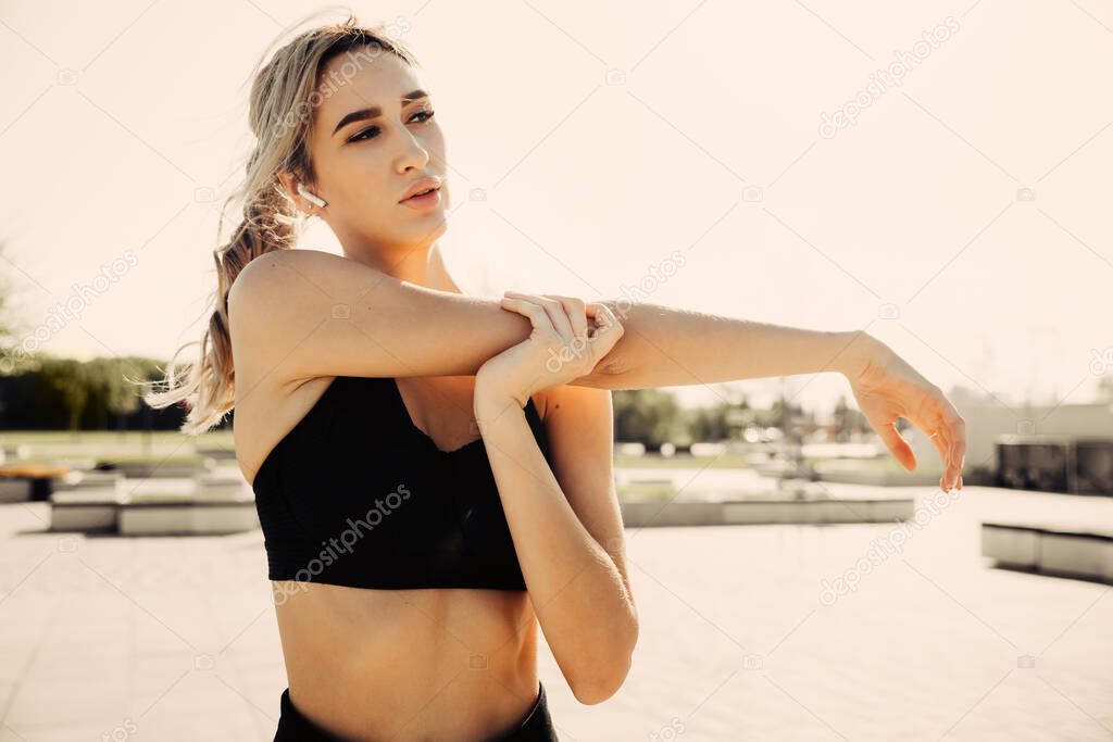 Portrait of a fitness woman doing warm up exercises outdoors, arm stretch.