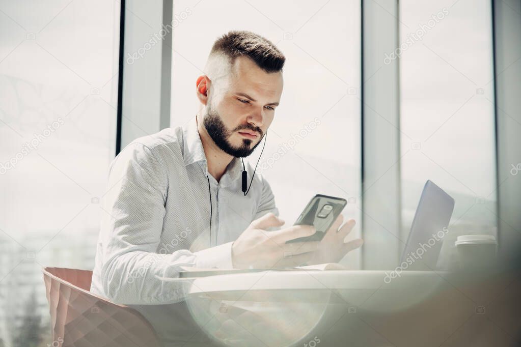 Young male businessman uses laptop and smartphone.