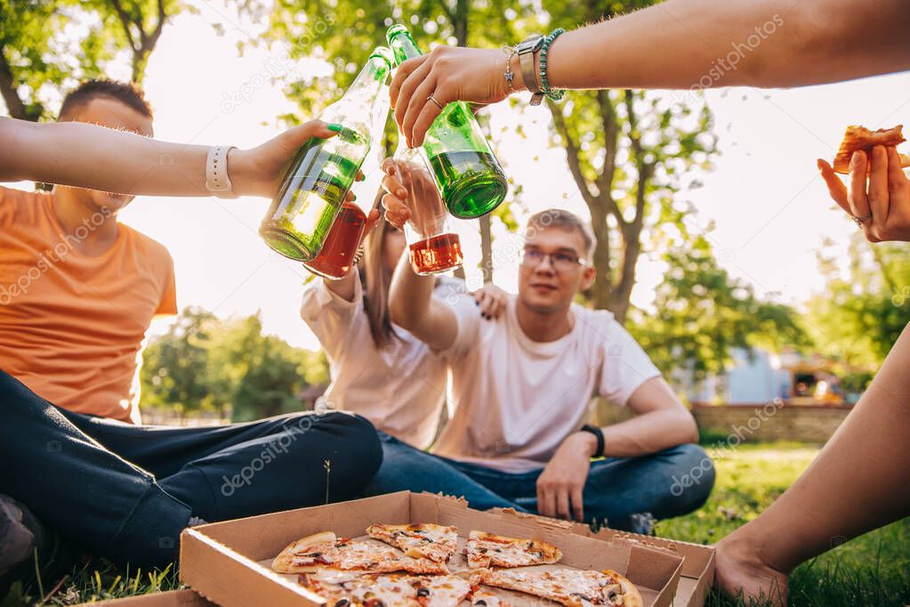 Friends drink beer and alcohol and eat pizza outdoors, hands close-up.