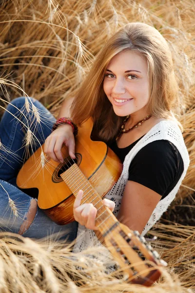 Schönes Mädchen spielt Gitarre in einem Weizenfeld — Stockfoto