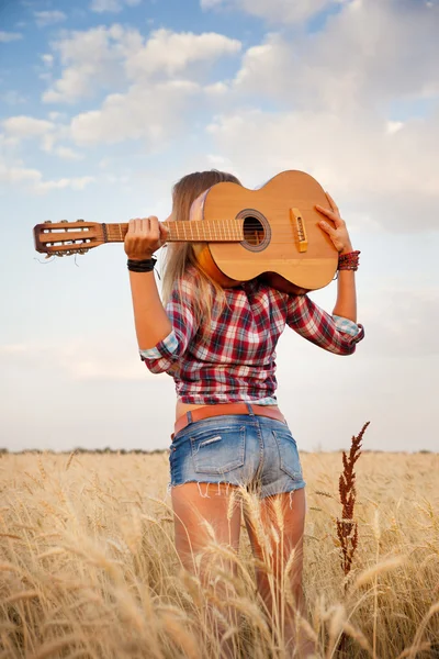 Piękna dziewczyna z gitarą w tle pole pszenicy, widok z tyłu — Zdjęcie stockowe