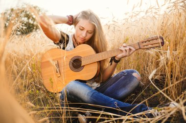 Güzel bir kız buğday tarlasında gitar çalıyor.