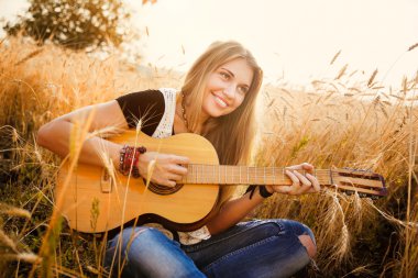 Güzel bir kız buğday tarlasında gitar çalıyor.