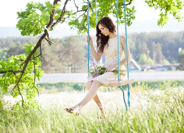 Jonge vrouw is swingend op een schommel in zomer bos. — Stockfoto