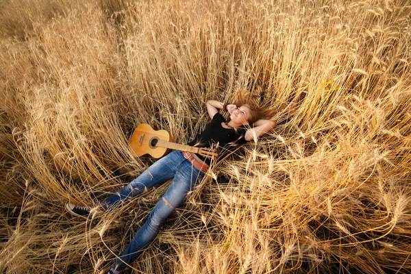 Meisje met een gitaar liggen in het tarweveld, bekijken van bovenaf — Stockfoto