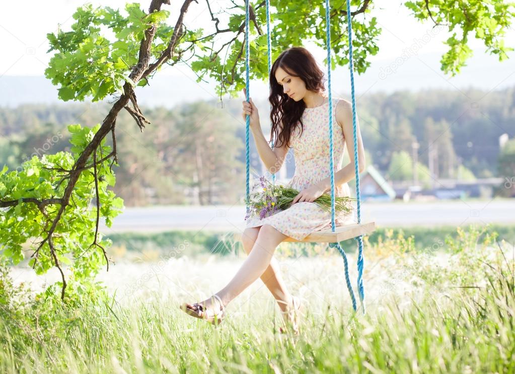 Young woman is swinging on a swing in summer forest.