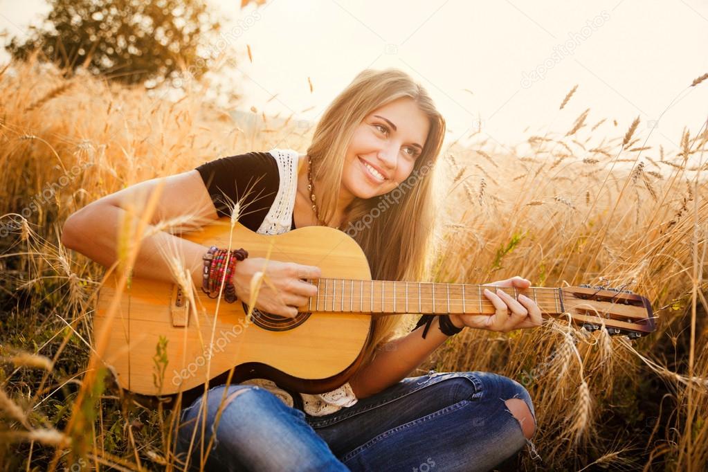 beautiful girl playing the guitar in a wheat field