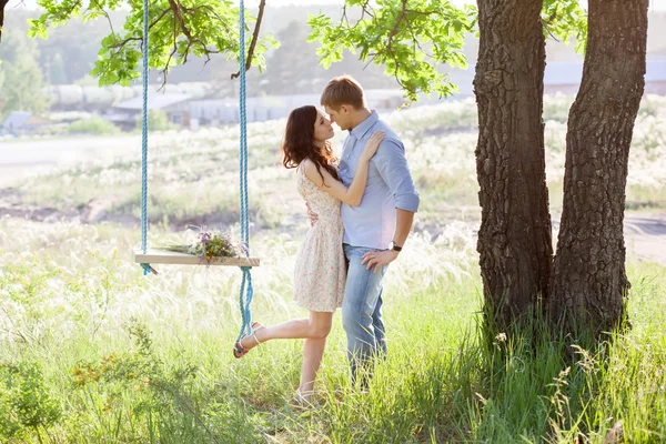 Young kissing couple under big tree with swing — Stock Photo, Image