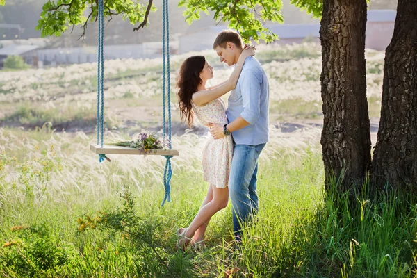 Young kissing couple under big tree with swing — Stock Photo, Image