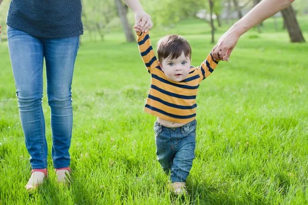 Primeros pasos. Bebé aprendiendo a caminar, con la ayuda de las manos de madres y padres . — Foto de Stock