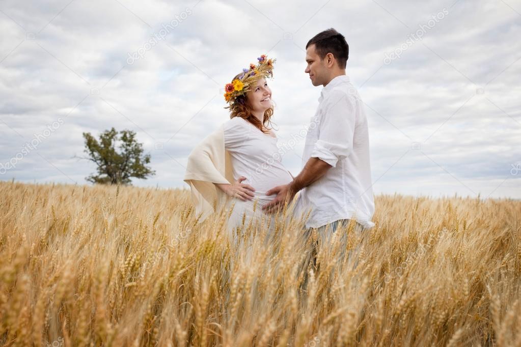 Outdoor portrait of young pregnant couple in field