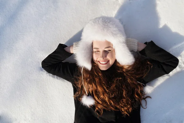 Glückliches Teenager-Mädchen, das an einem schönen Wintertag im Tiefschnee liegt. — Stockfoto