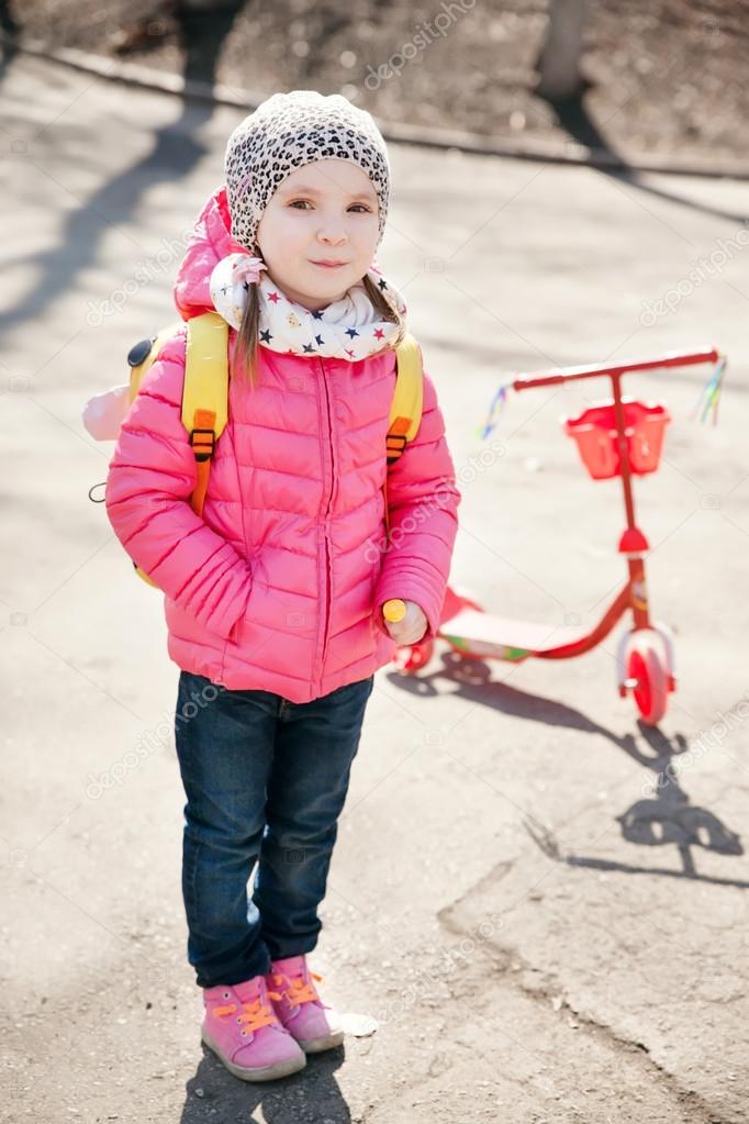 Portrait of cute toddler girl in pink jacket with the scooter
