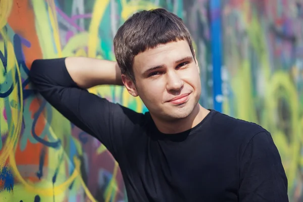 Atractivo joven de pie contra la colorida pared de graffiti — Foto de Stock