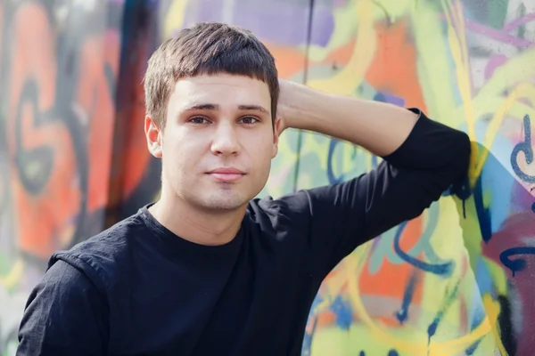 Aantrekkelijke jonge man permanent tegen kleurrijke graffiti muur, close-up — Stockfoto