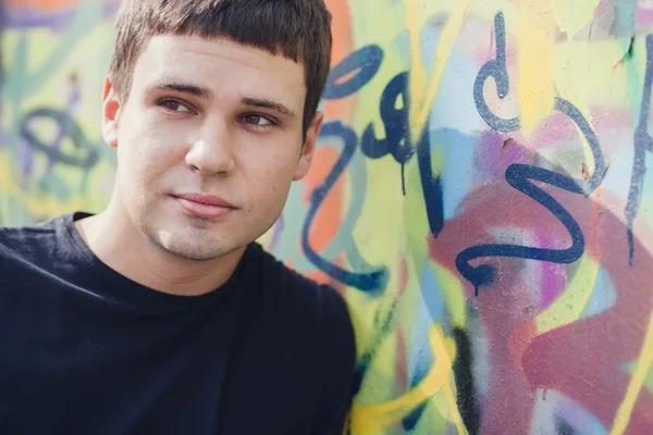 Jovem atraente em pé contra a parede de grafite colorido, close-up — Fotografia de Stock