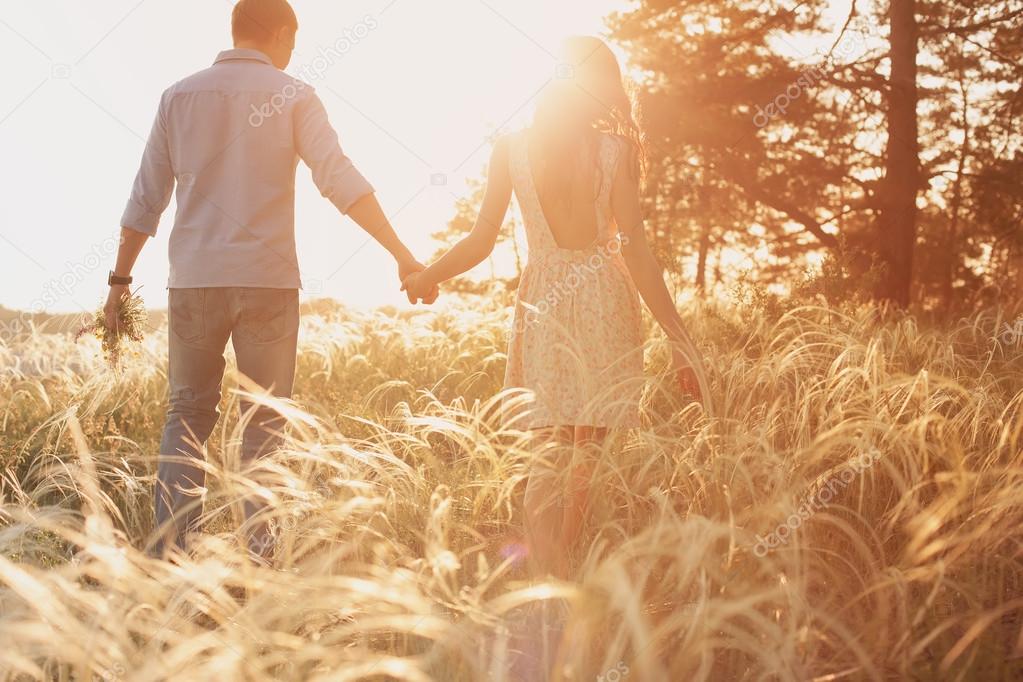 lovers walking in a field at sunset holding hands