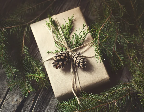 Handgefertigtes Geschenk auf rustikalem Holzgrund mit Tannenzweigen und Zapfen — Stockfoto