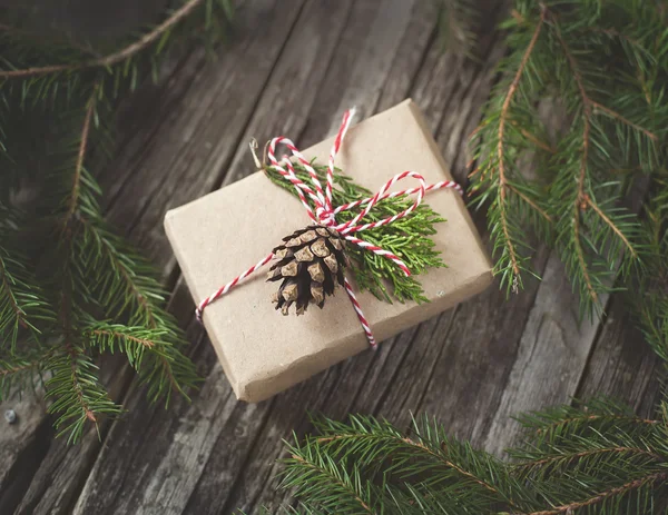 Hand crafted gift on rustic wooden background with with fir branches and cones — Stock Photo, Image