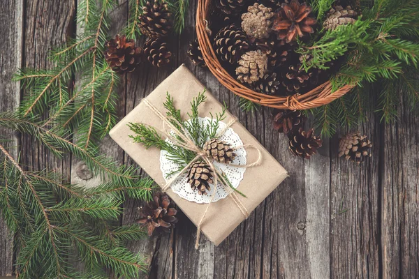 Cadeau artisanal sur fond bois rustique et un panier avec branches et cônes de sapin — Photo