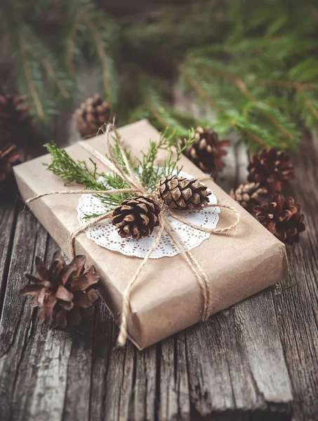 Hand crafted gift on rustic wooden background with with fir branches and cones — Stock Photo, Image
