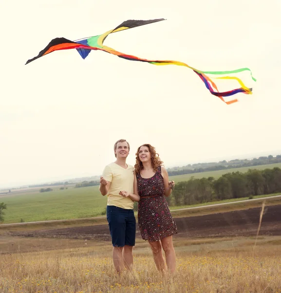 Feliz joven pareja enamorada de volar una cometa en el campo — Foto de Stock
