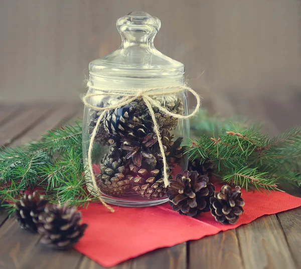 Pine cones in a glass jar on rustic wooden table, — Stock Photo, Image