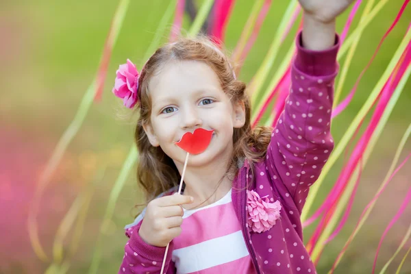 Little girl holding paper lips on a stick — Stock Photo, Image