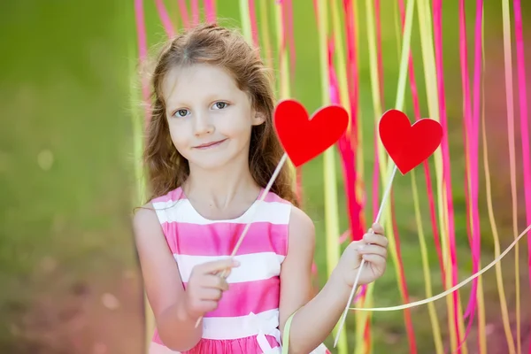 Kleines Mädchen in der festlichen Dekoration im Garten, das Herzen hält — Stockfoto