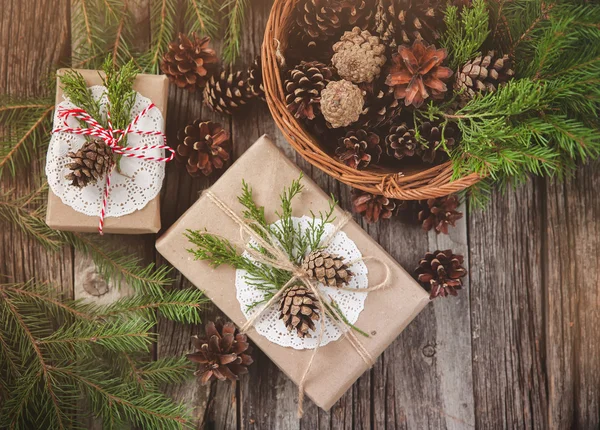 Hand crafted gift on rustic wooden background and a basket with fir branches and cones, top view — Stock Photo, Image