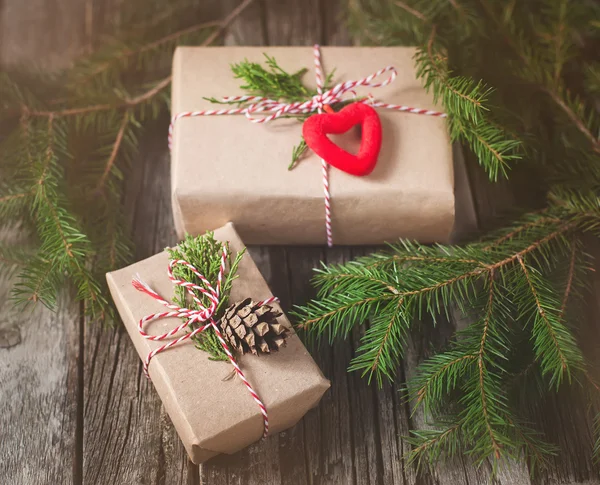 Hand crafted gift on rustic wooden background with with fir branches and cones, toned image — Stock Photo, Image