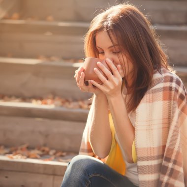Dinlenme ve sonbahar Bahçe yünlü ekose battaniyeye sarılmış basamaklarda oturup çay içme genç kadın.
