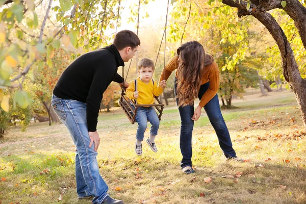 Ευτυχισμένη οικογένεια διασκεδάζοντας μια ταλάντευση βόλτα σε ένα κήπο μια φθινοπωρινή μέρα — Φωτογραφία Αρχείου