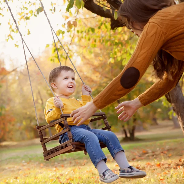 Fröhlicher kleiner Junge, der an einem Herbsttag Spaß auf einer Schaukelfahrt im Garten hat — Stockfoto