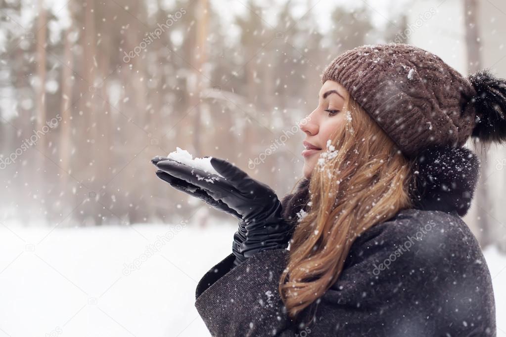 girl outdoor portrait. Winter woman blowing snow in a park, closeup