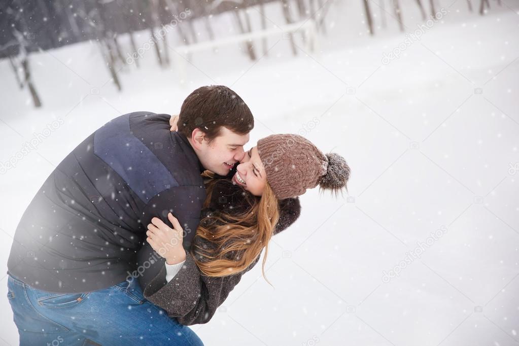 Young couple in love in the winter forest. Young man embraces the girl. She laughs.