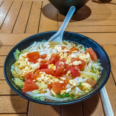 Geleneksel Çin erişte çorbası lahana, domates, tavuk ve yumurta ile siyah tabakta Sanya Nanshan Kültür Merkezi 'nde pişirildi.