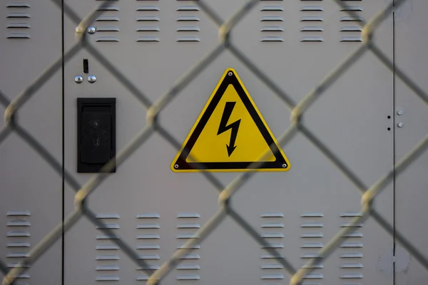 Electrical hazard sign placed on an electric power substation behind a metal fence of wire mesh, sanctions, restrictions — Stock Photo, Image