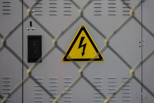 Знак електричної небезпеки, встановлений на електричній підстанції за металевим парканом з дротяної сітки, санкції, обмеження Стокова Картинка