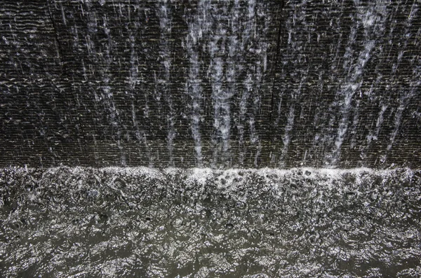 Fluindo água da folha da cachoeira artificial ao longo da parede de concreto áspero — Fotografia de Stock