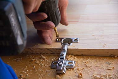  Tahtası, delikleri ve kapı menteşesi ve talaşı olan elektrikli el matkabı kullanan bir adam.