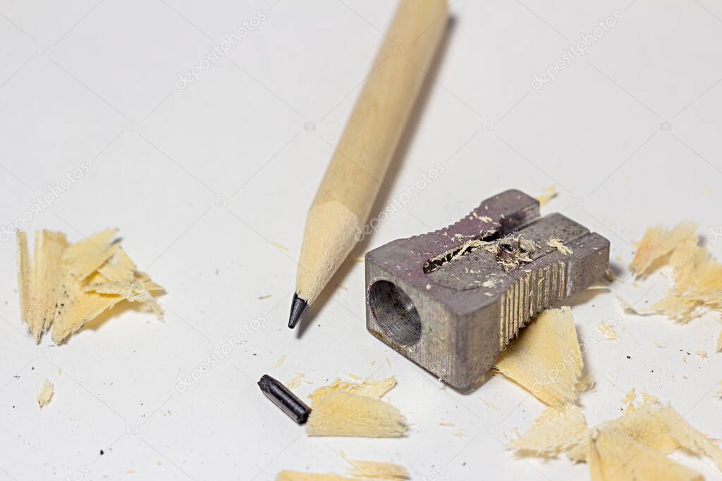 Broken pencil with metal sharpener, broken lead rod and shavings on white paper background