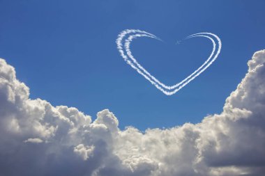 Derin mavi gökyüzünde beyaz bulutların üzerinde uçar ve kalp şeklinde jet izleri bırakır.