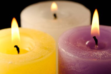 Siyah arka planda, beyaz, sarı ve eflatun renkli üç kalın hatıra, yakın plan makro fotoğrafında yanıyor.