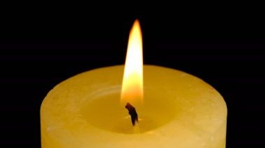 Büyük, kalın, sarı bir mum, siyah arka planda yüksek çözünürlüklü video klipte yakın çekim yapıyor.