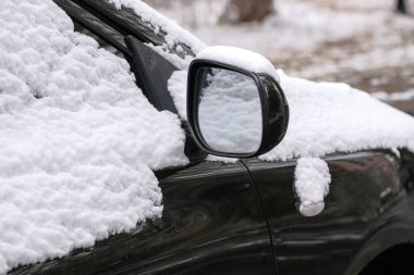 Siyah bir yolcu arabası şehrin yerleşim yerinin yakınına park edilmiş. İlk sonbahar kar yağışlı yakın çekim parçasıyla kaplı.