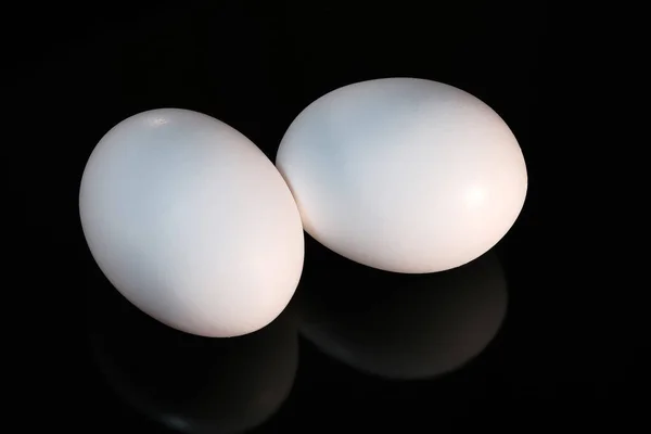 Dwa Białe Surowe Jaja Kurze Leżą Czarnym Odblaskowym Tle Zbliżenie — Zdjęcie stockowe