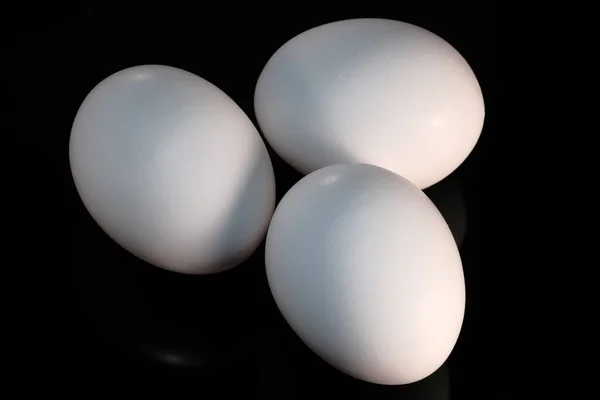 Trzy Białe Surowe Jaja Kurze Leżą Czarnym Odblaskowym Tle Zbliżenie — Zdjęcie stockowe