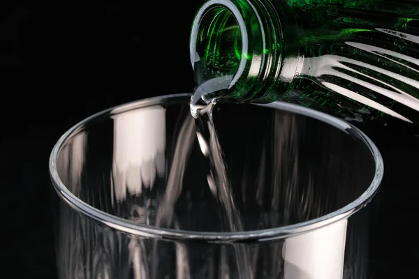 黒の背景に透明なガラスに瓶から注ぐ純炭酸水クローズアップマクロ写真 — ストック写真