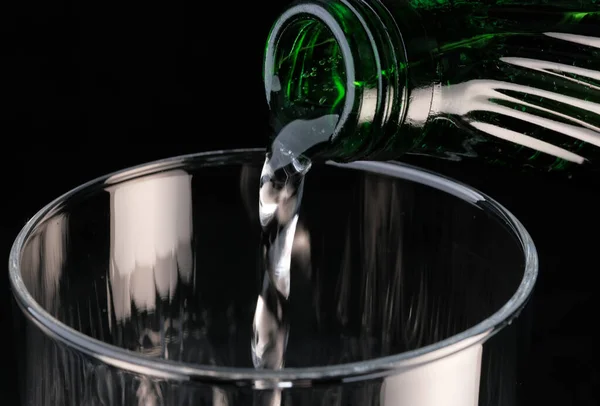 黒の背景に透明なガラスに瓶から注ぐ純炭酸水クローズアップマクロ写真 — ストック写真